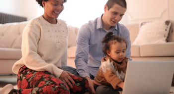 Image of two adults and a child sitting on the floor with a laptop