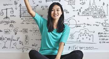 Image of a woman raising her hand in front of a whiteboard covered in drawings